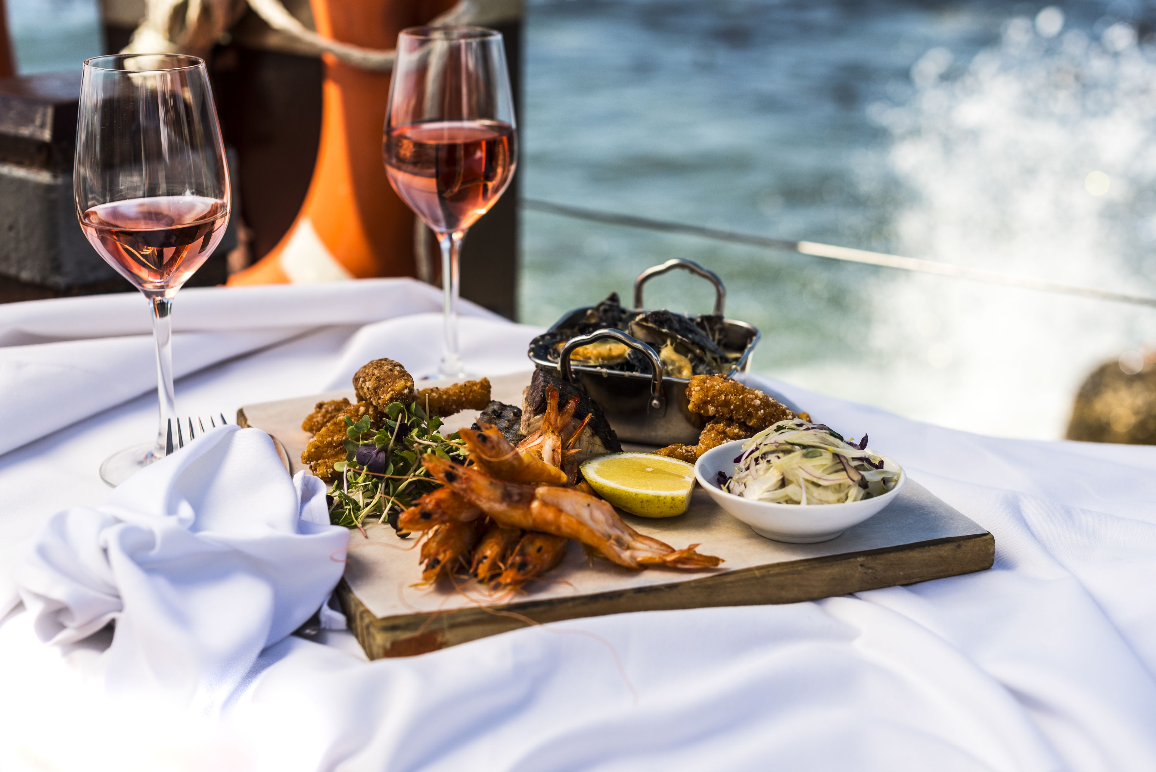 A table with seafood, a glass of wine, and a view of the ocean.