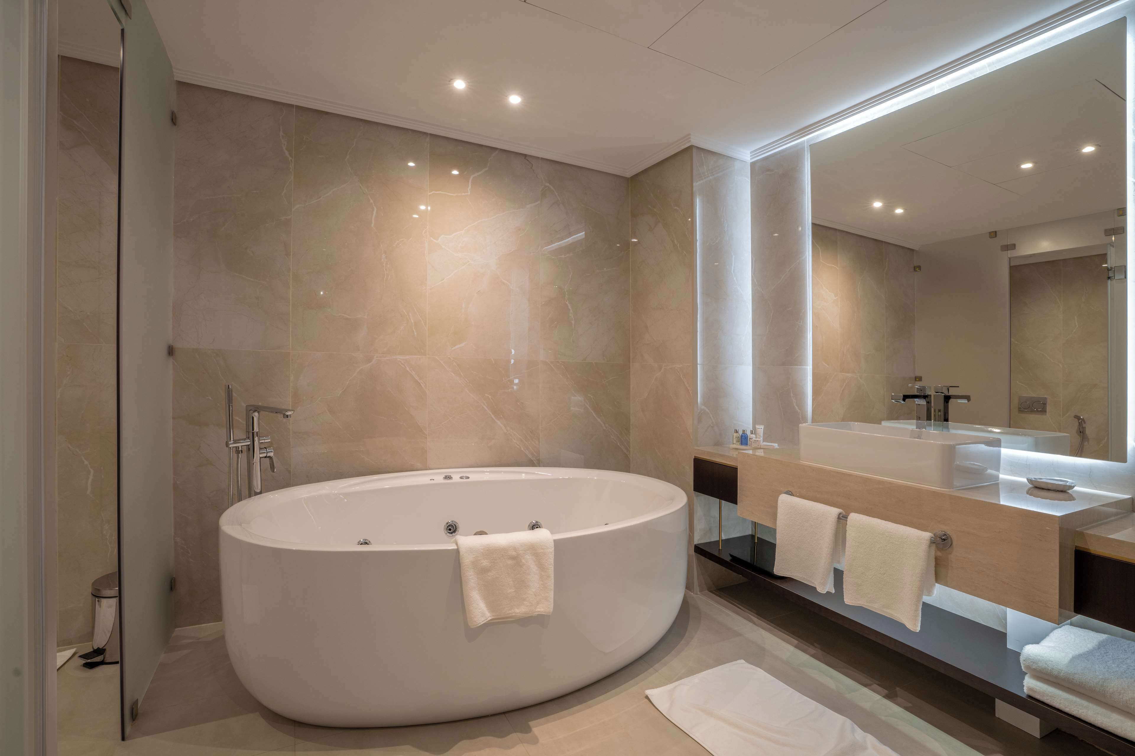A modern bathroom with a large oval bathtub, a glass-enclosed shower, and a large mirror above the sink.
