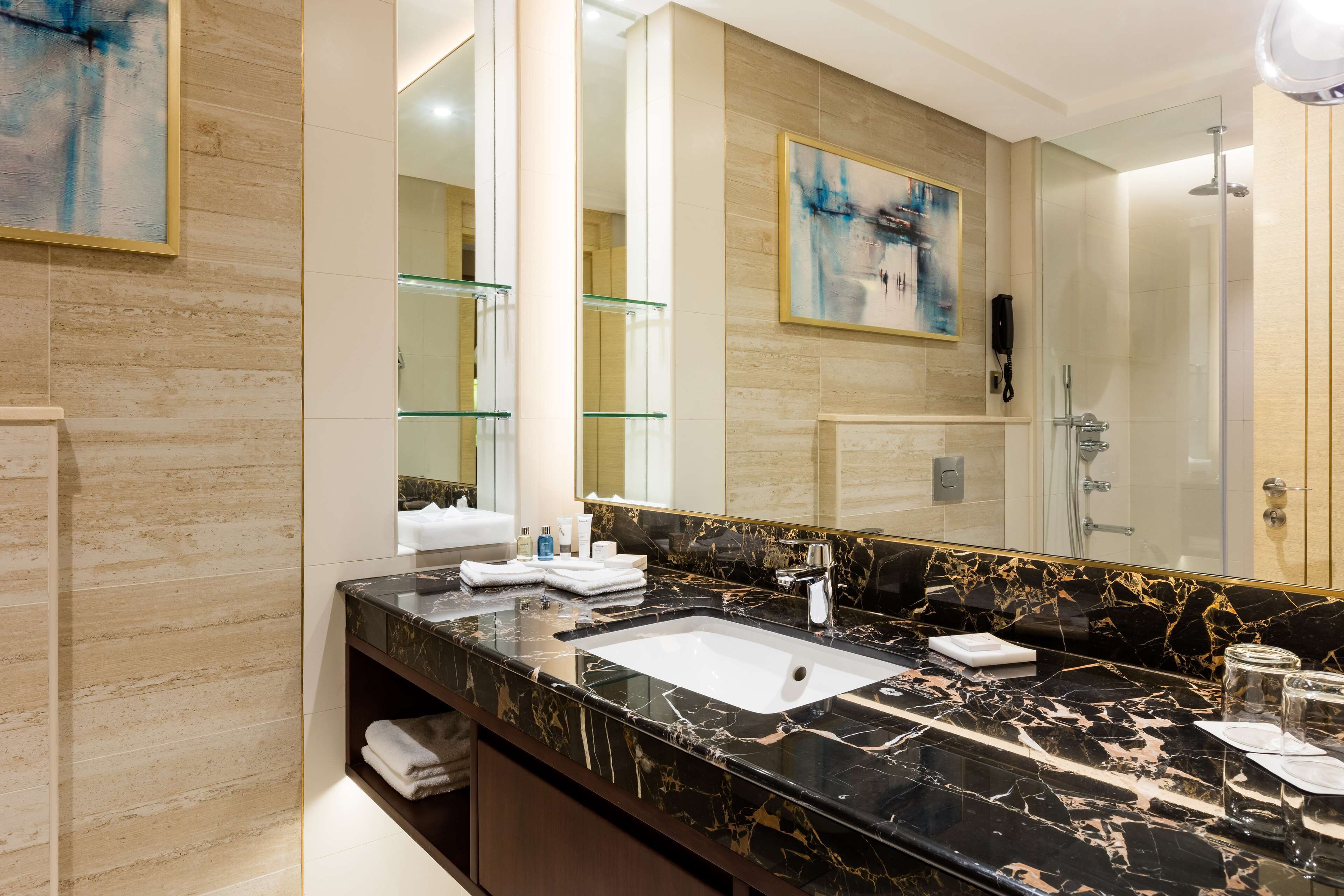 A modern bathroom with a large mirror, marble countertop, and a glass shower enclosure.