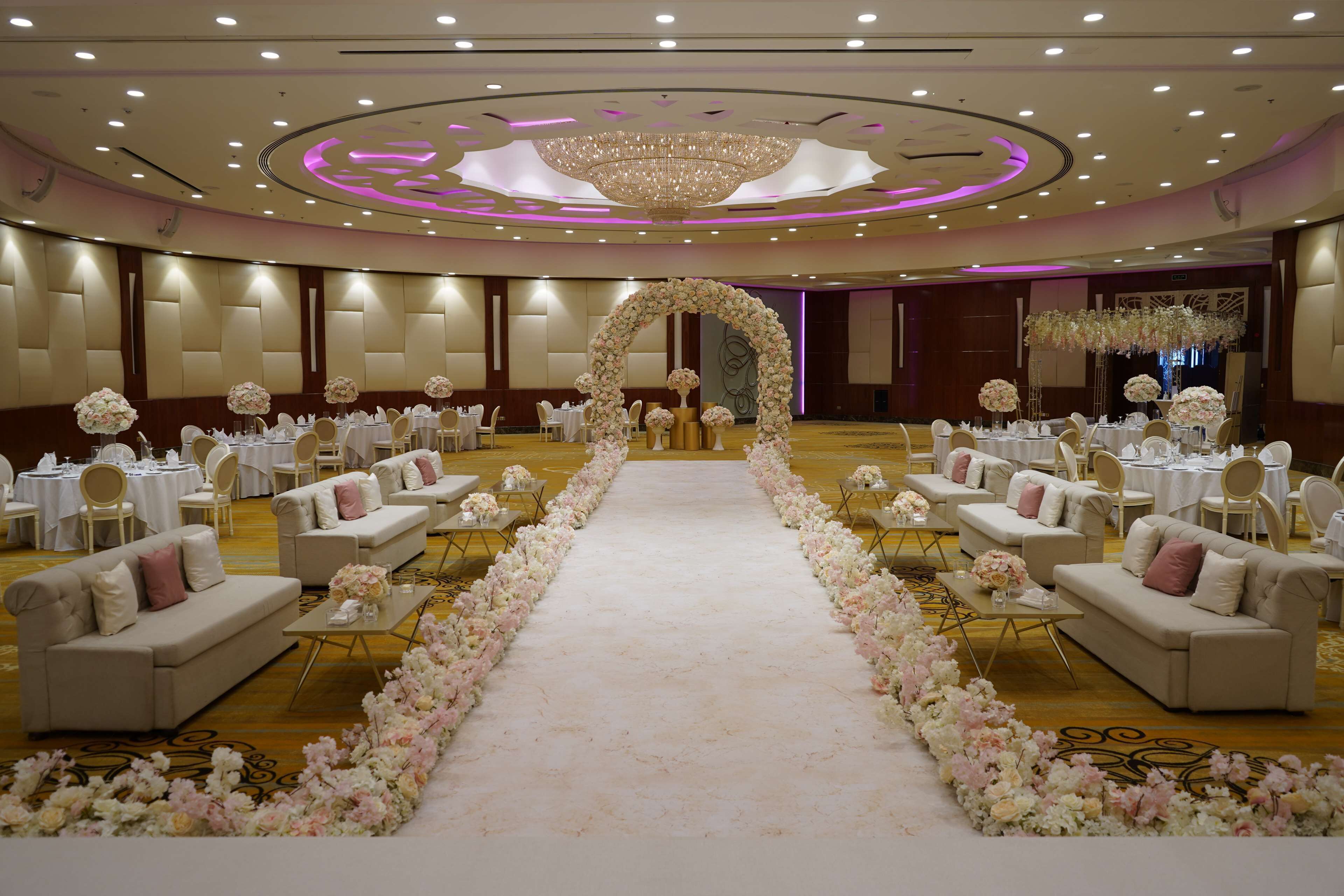 A hotel ballroom with a central aisle, round tables, and sofas arranged around it.