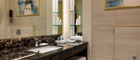 A modern bathroom with a black marble sink, a large mirror, and two glass shelves with toiletries.