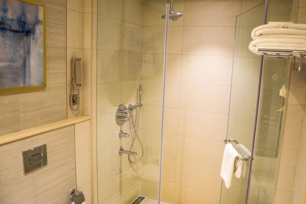 A glass-enclosed shower with a handheld showerhead, a handheld showerhead, and a towel rack with a towel.