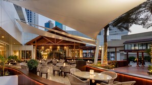 An outdoor dining area with wicker furniture, a bar, and a large canopy. - The Diplomat Radisson BLU Hotel, Residence & Spa (Manama)