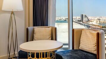Hotelkamer met een groot raam, een ronde tafel, twee fauteuils, een vloerlamp en een kamerbreed tapijt met dessin.