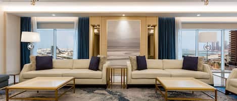 A modern hotel lobby with two sofas facing a large window, a central coffee table, and a chandelier.