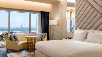A hotel room with a large bed, a sofa, a small round table, and a large window offering a city view.