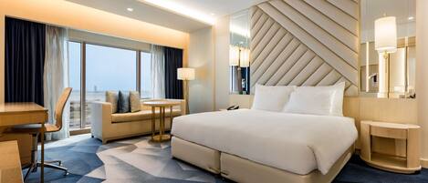 A modern hotel room with a large bed, a desk, a sofa, and a view of the city.