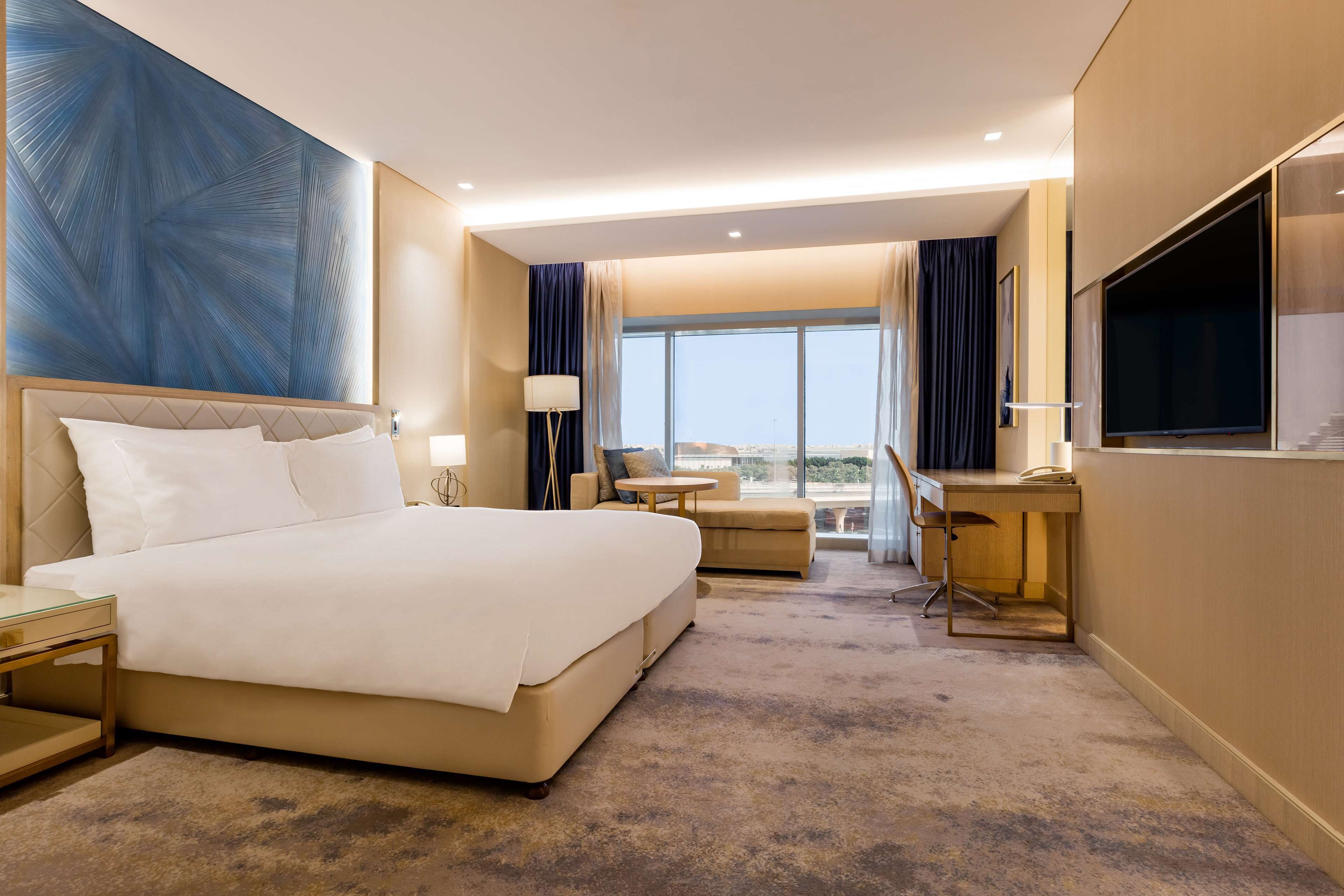 A hotel room with a large bed, a desk, a chair, and a TV.