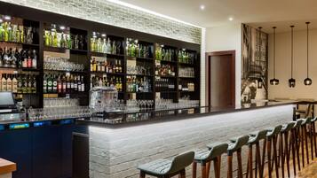 A bar area with a brick wall, shelves of bottles, glasses, and a long counter with bar stools.