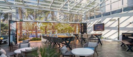 An indoor/outdoor dining area with glass walls, tables, and chairs.