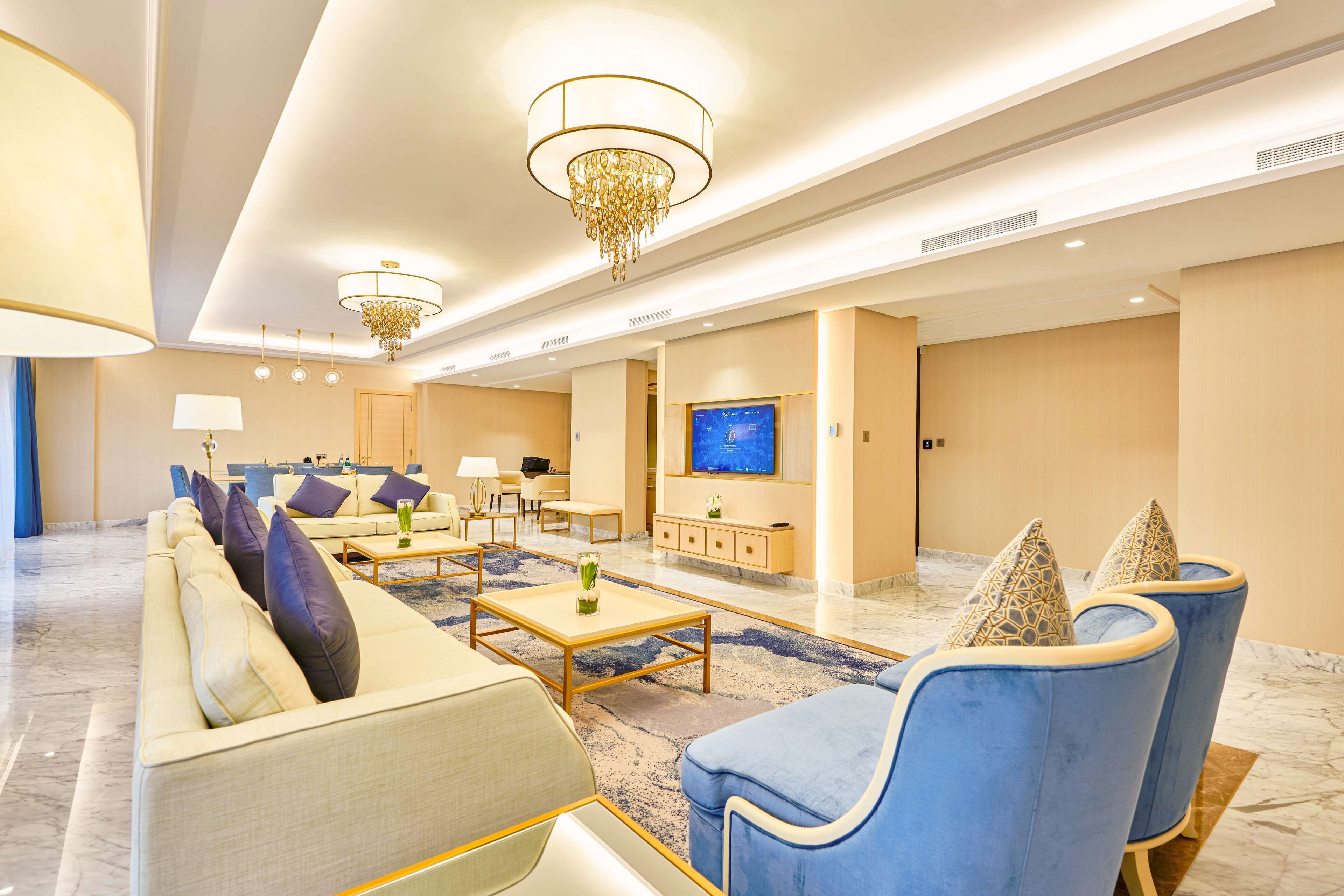 Eine großzügige Lobby mit einer Couch, Sesseln, einem Couchtisch und einem Fernseher.