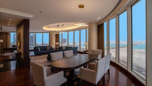 A spacious hotel room with a large dining table, comfortable seating, a sofa, and a view of the cityscape through large windows. - The Diplomat Radisson BLU Hotel, Residence & Spa (Manama)