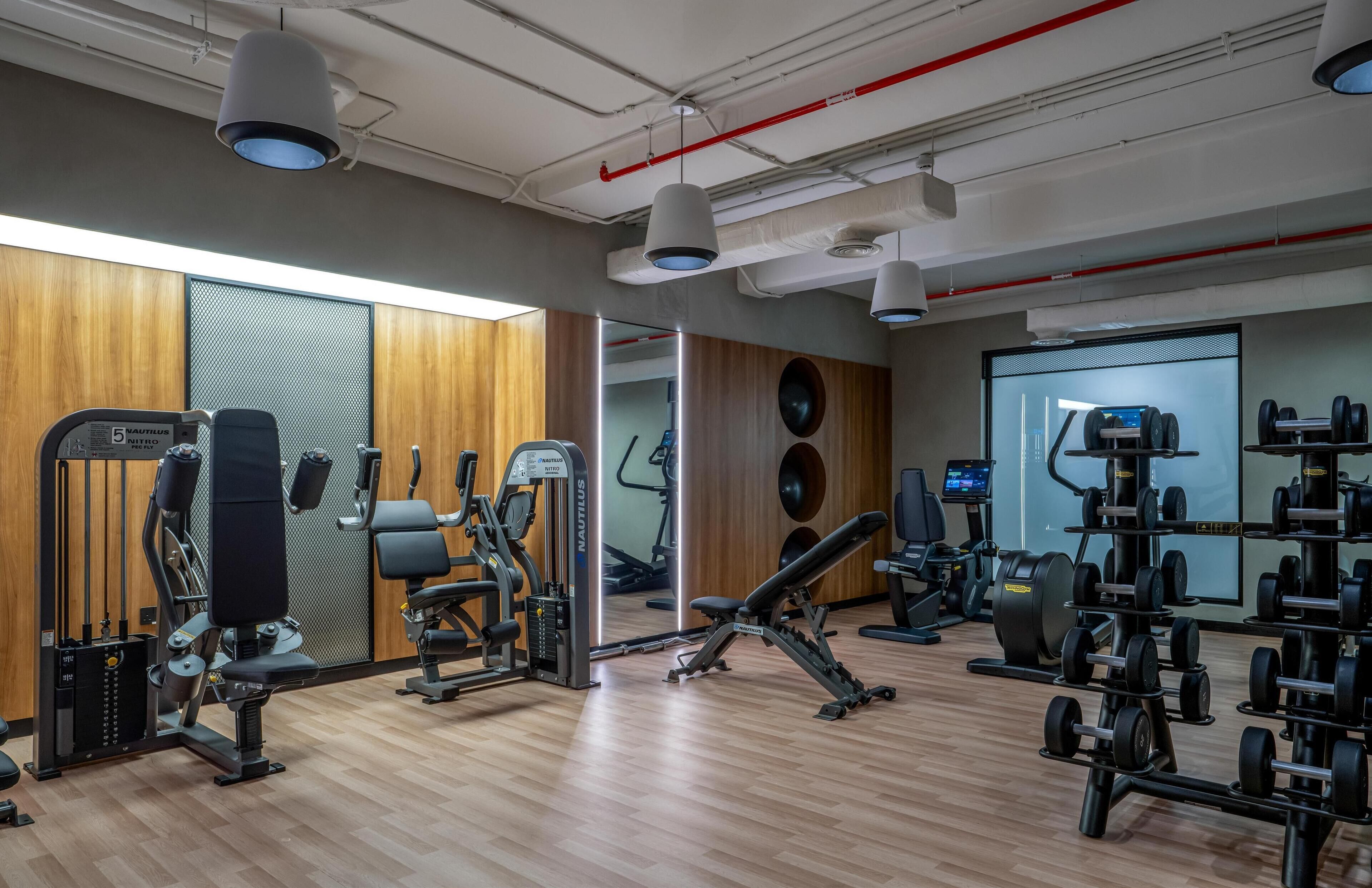 A modern gym with various exercise equipment, wooden flooring, and a large mirror.