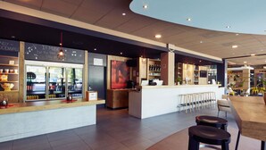 A modern bar area with a counter, stools, and a large poster on the wall. - ibis Zurich Messe-Airport (Zürich)