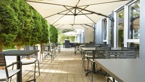 An outdoor patio area with tables and chairs, a covered seating area, and a view of the surrounding landscape. - ibis Zurich Messe-Airport (Zürich)