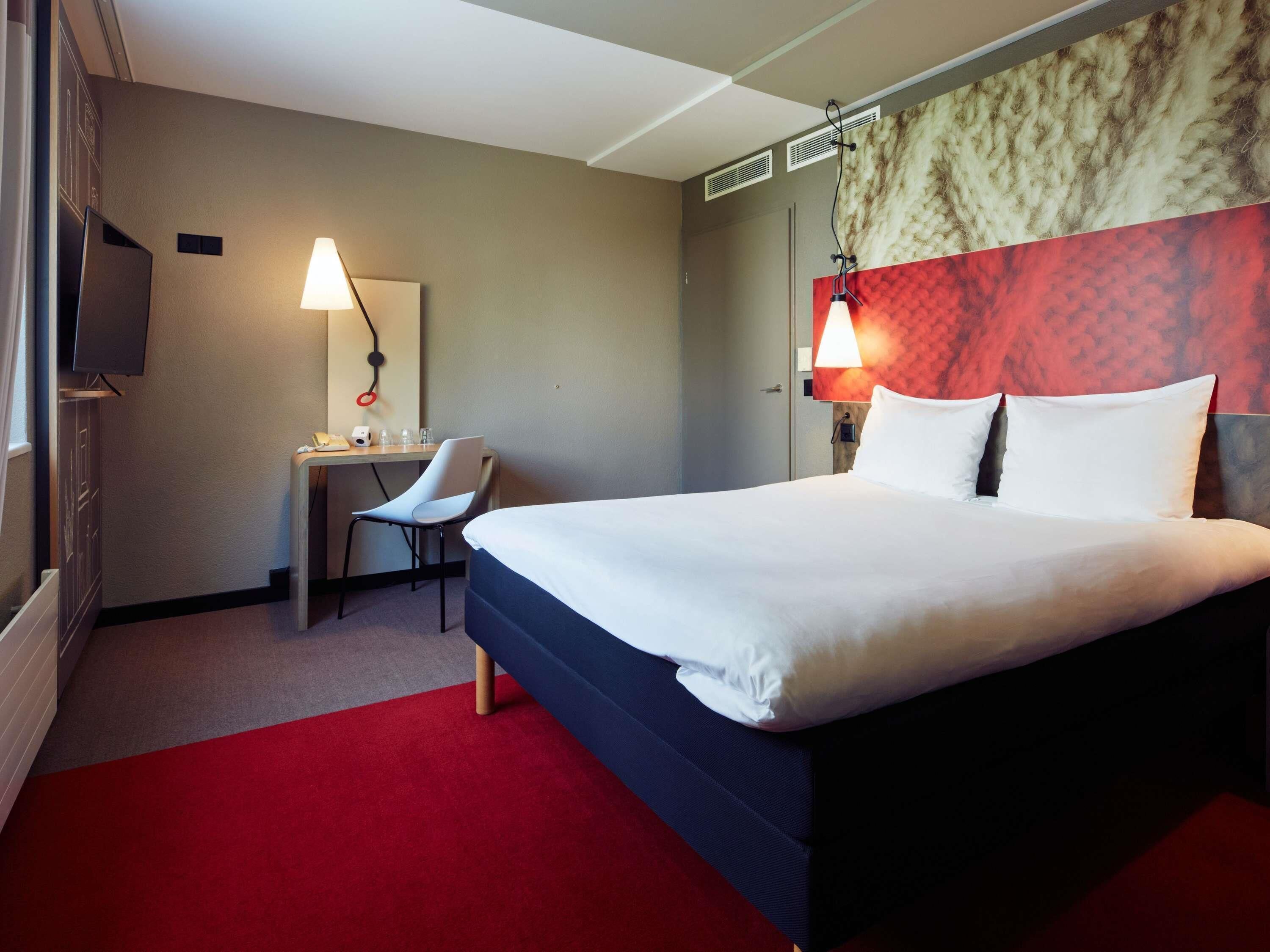 A hotel room with a bed, desk, chair, and a television.