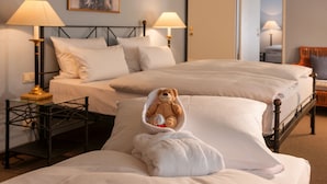 Habitación de hotel con dos camas, una mesita de noche con lámparas y un oso de peluche sobre una de las camas.