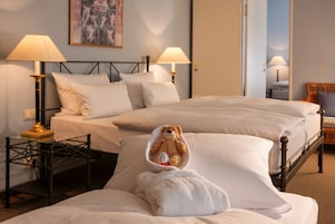 A hotel room with two beds, a bedside table with lamps, and a teddy bear on one bed.