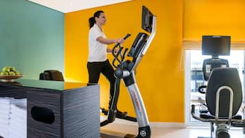 Una habitación de hotel moderna con un ventanal grande, una cinta de correr y un escritorio con un frutero.