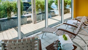 Una terraza soleada con sillones de mimbre, una mesa de madera con una toalla y botellas, y vistas a zonas verdes y edificios.