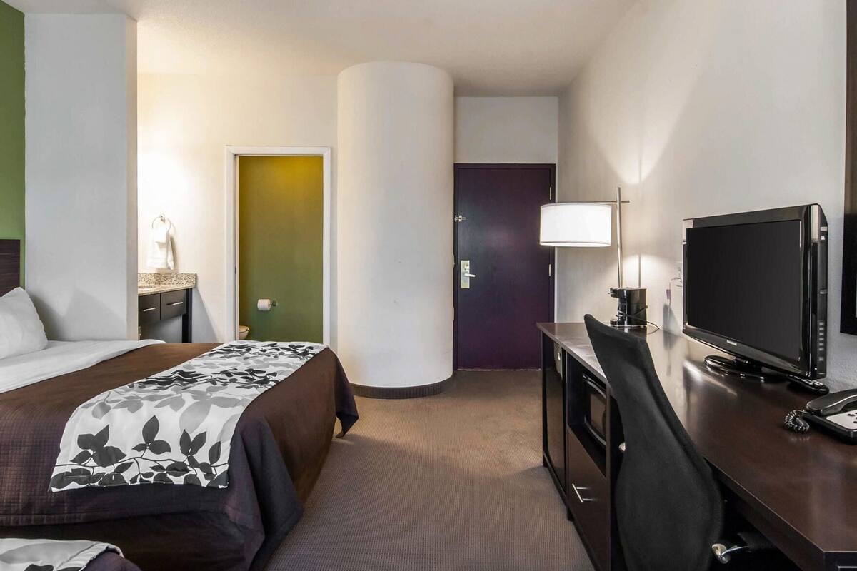 A hotel room with a bed, desk, television, and a door leading to another room.