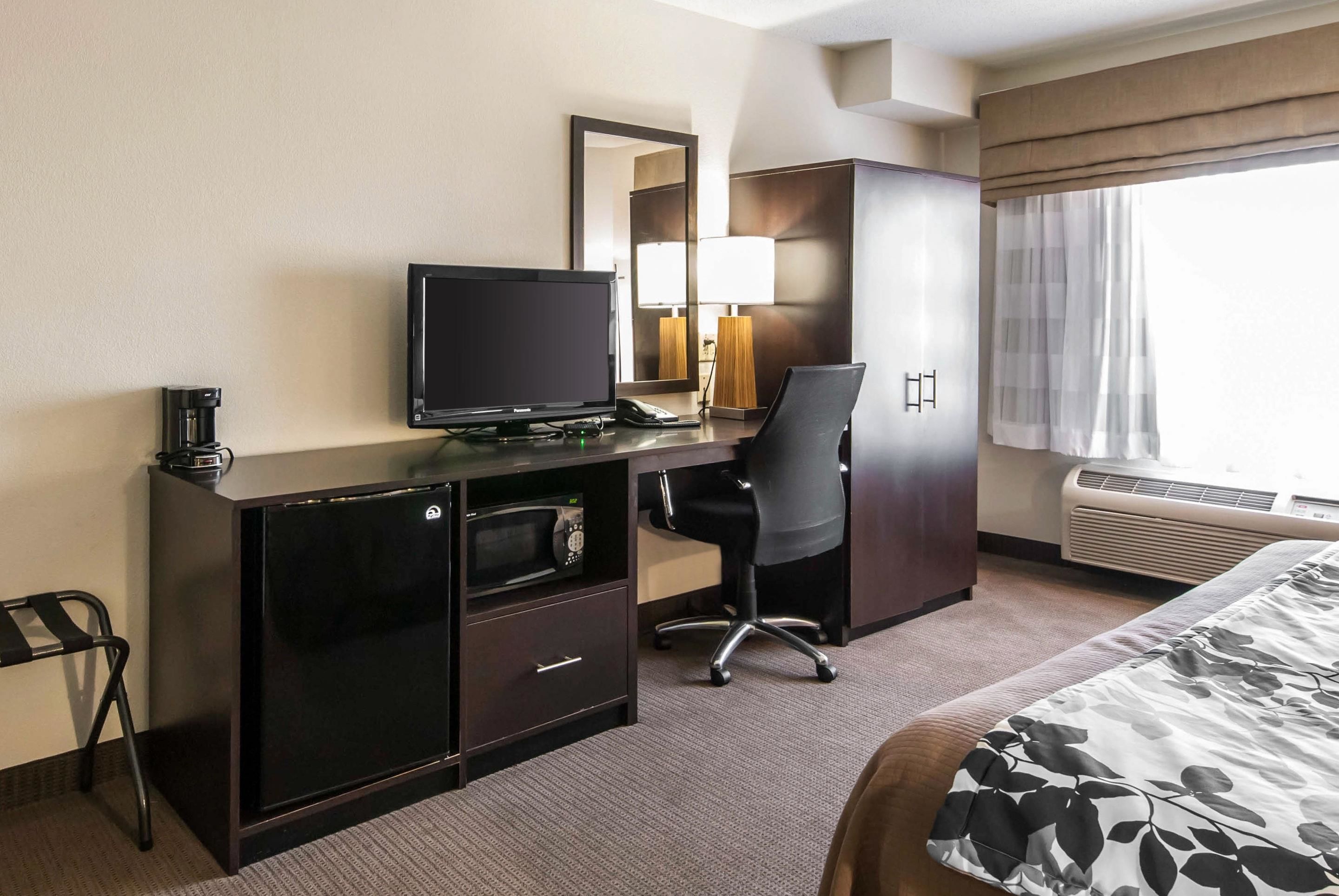 Une chambre d’hôtel comprenant un lit, un bureau avec un ordinateur, une chaise, un four à micro-ondes, une lampe et un grand miroir.