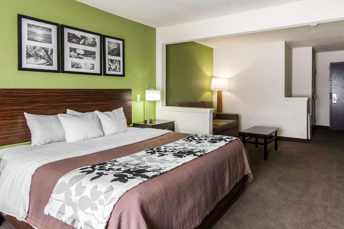 A hotel room with a bed, a nightstand, a lamp, a chair, and a door.