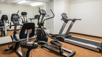 Un gimnasio con máquinas de cardio, un espejo grande y suelo cubierto de alfombra.