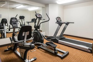 Un gimnasio con máquinas de cardio, un espejo grande y suelo cubierto de alfombra.