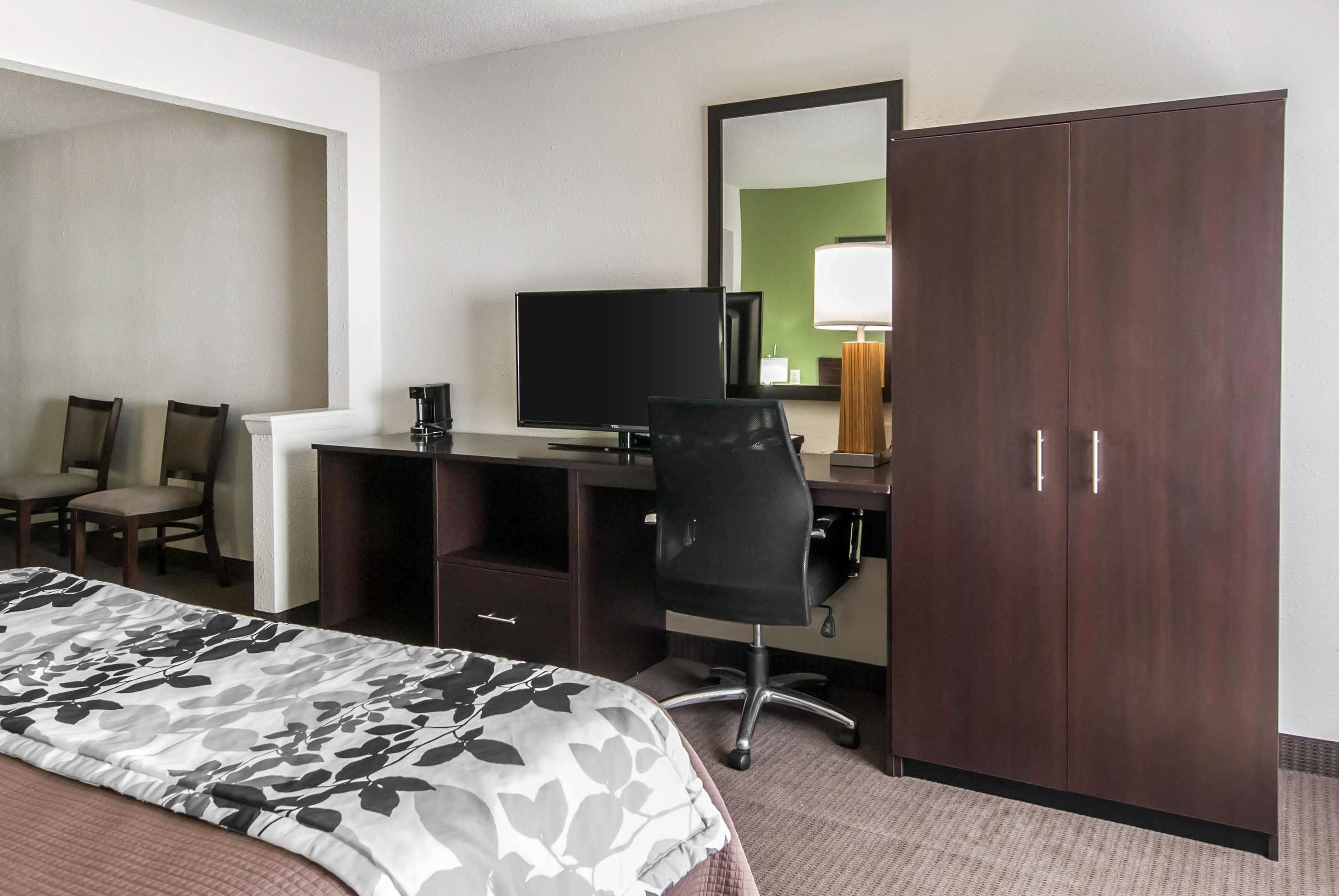 A hotel room with a bed, a desk with a computer, a chair, a wardrobe, and a television.