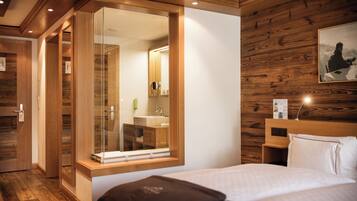 Habitación de hotel con pared de madera, un espejo grande, una cama con ropa blanca y una mesita de noche de madera.
