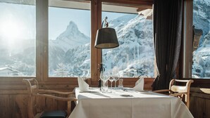 A dining table set with chairs, a lamp, and a mountain view. - Relais & Chateaux Schönegg (Zermatt)