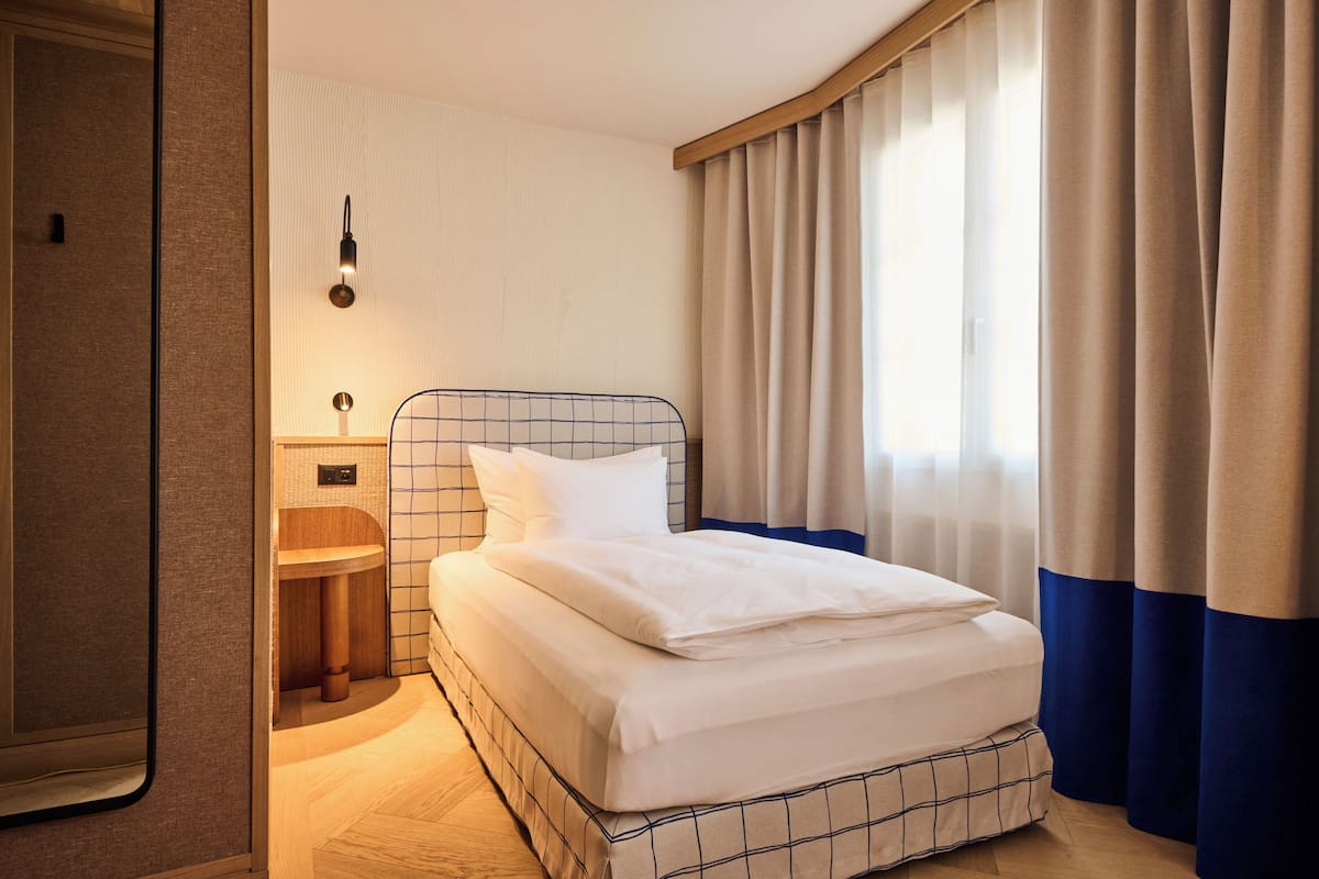 A neatly made bed with a headboard, a bedside table, and a wall-mounted light fixture in a hotel room.