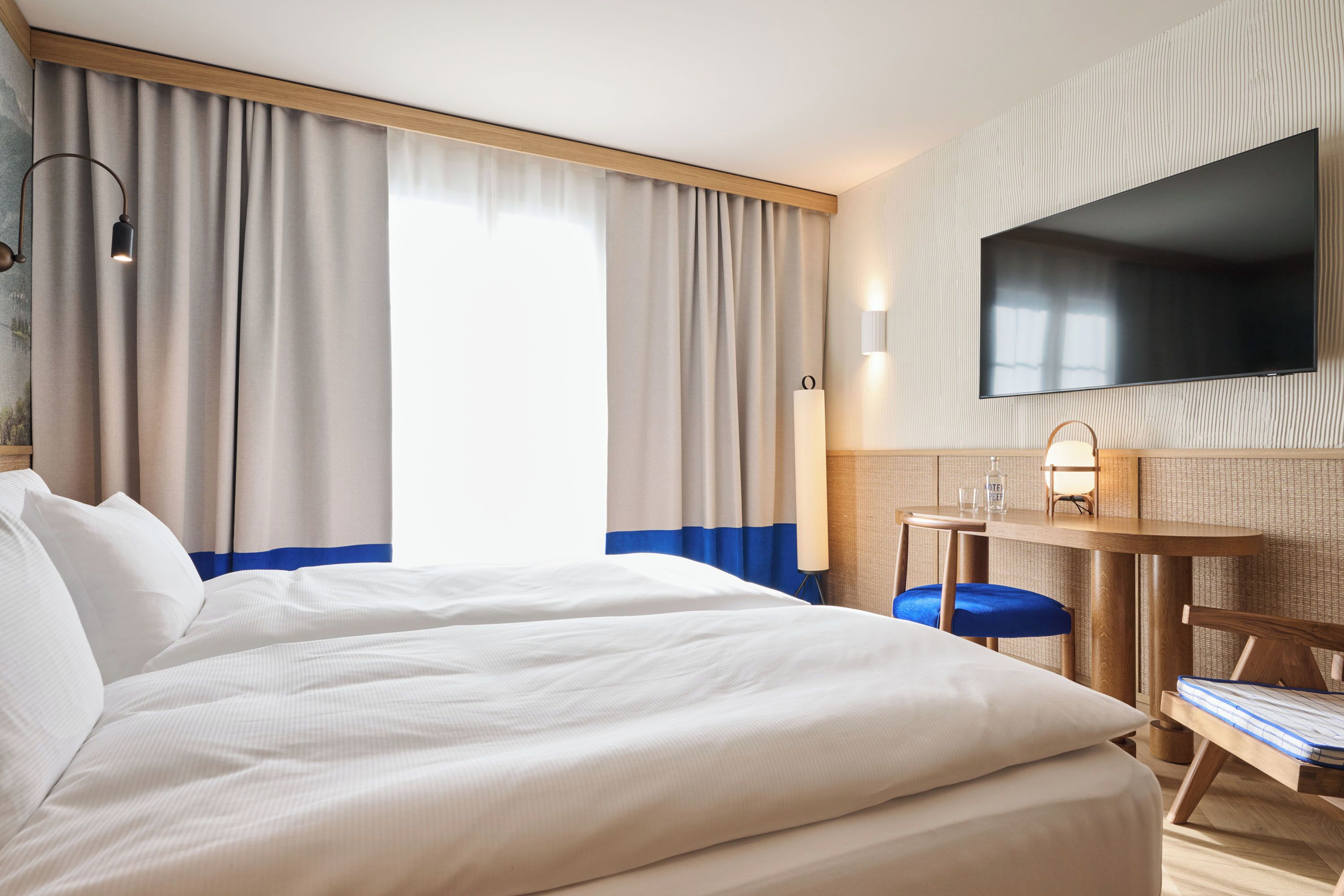 Una habitació d'hotel amb un llit gran, un escriptori amb una cadira, una televisió penjada a la paret i cortines a les finestres.