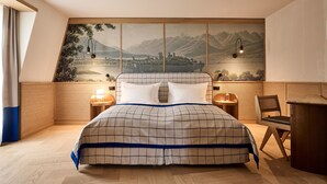 A bedroom with a bed, two bedside tables, a chair, a desk, and a large wall mural. - Sorell Boutique-Hotel Speer Rapperswil (Rapperswil-Jona)