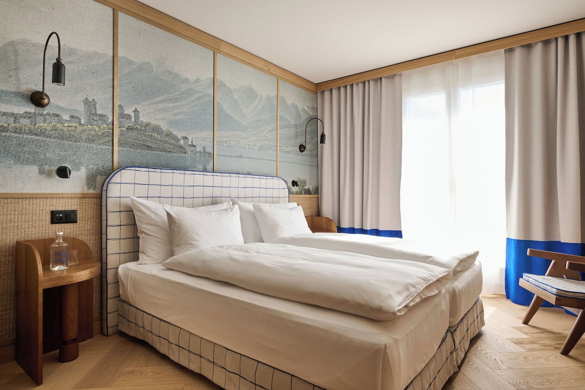 A neatly made bed with white linens, a wooden headboard, and a nightstand with a bottle and glass.