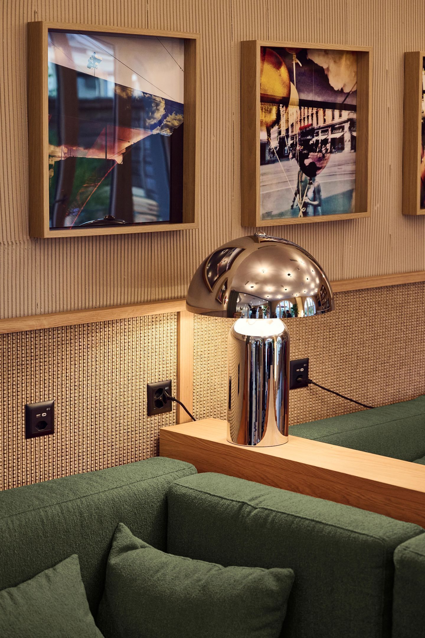 A modern interior with a green sofa, a metallic lamp, and framed artwork on the wall.