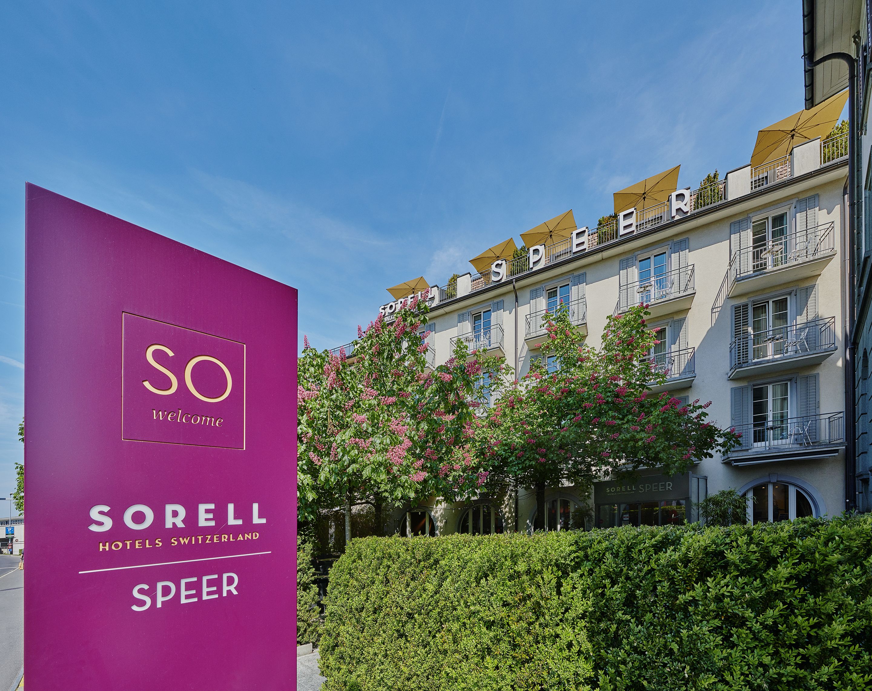 Entrada de un hotel con un gran letrero púrpura que dice "Sorell Hotels Switzerland Speer".