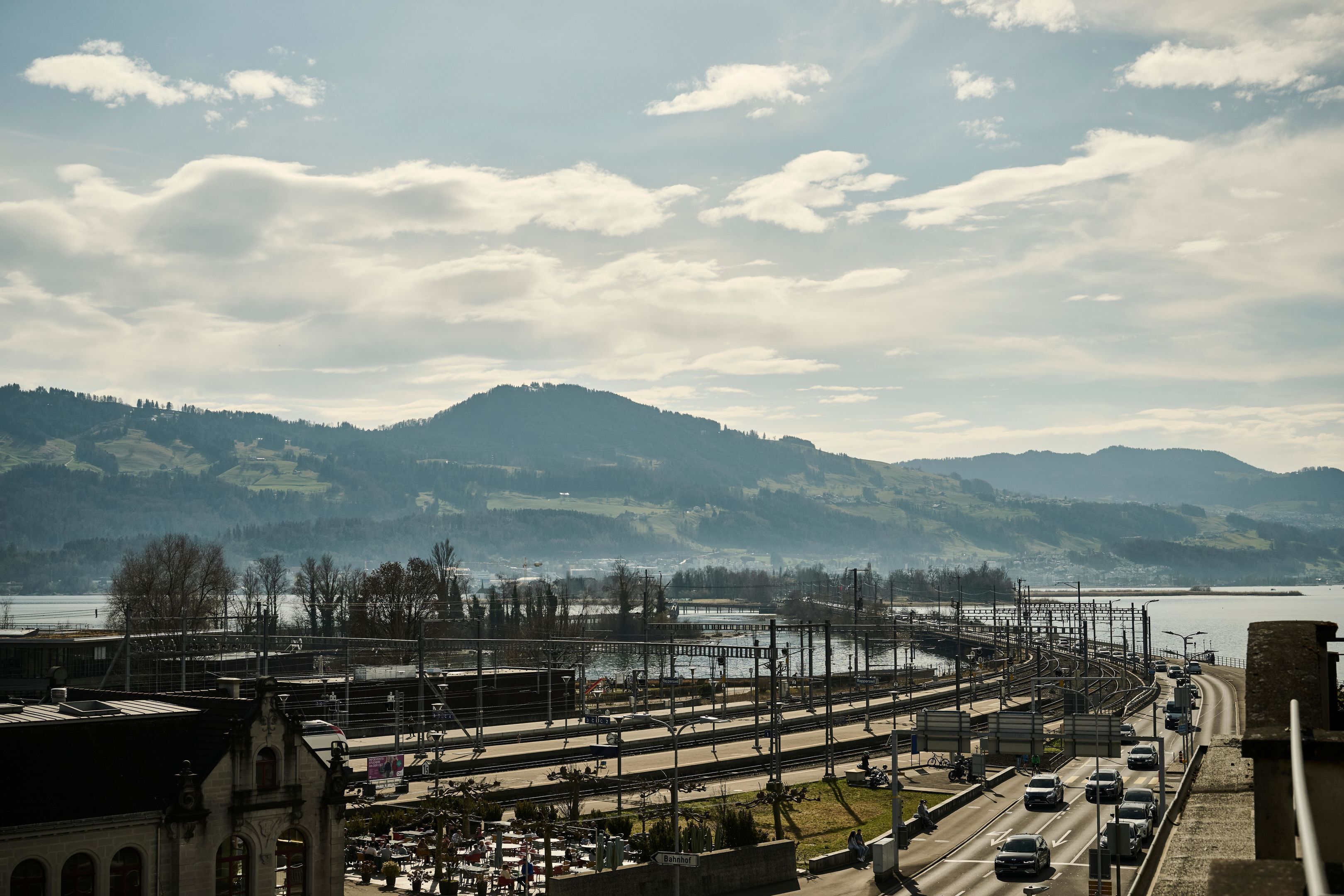 A railway station with multiple tracks, a bridge, and a body of water in the background.