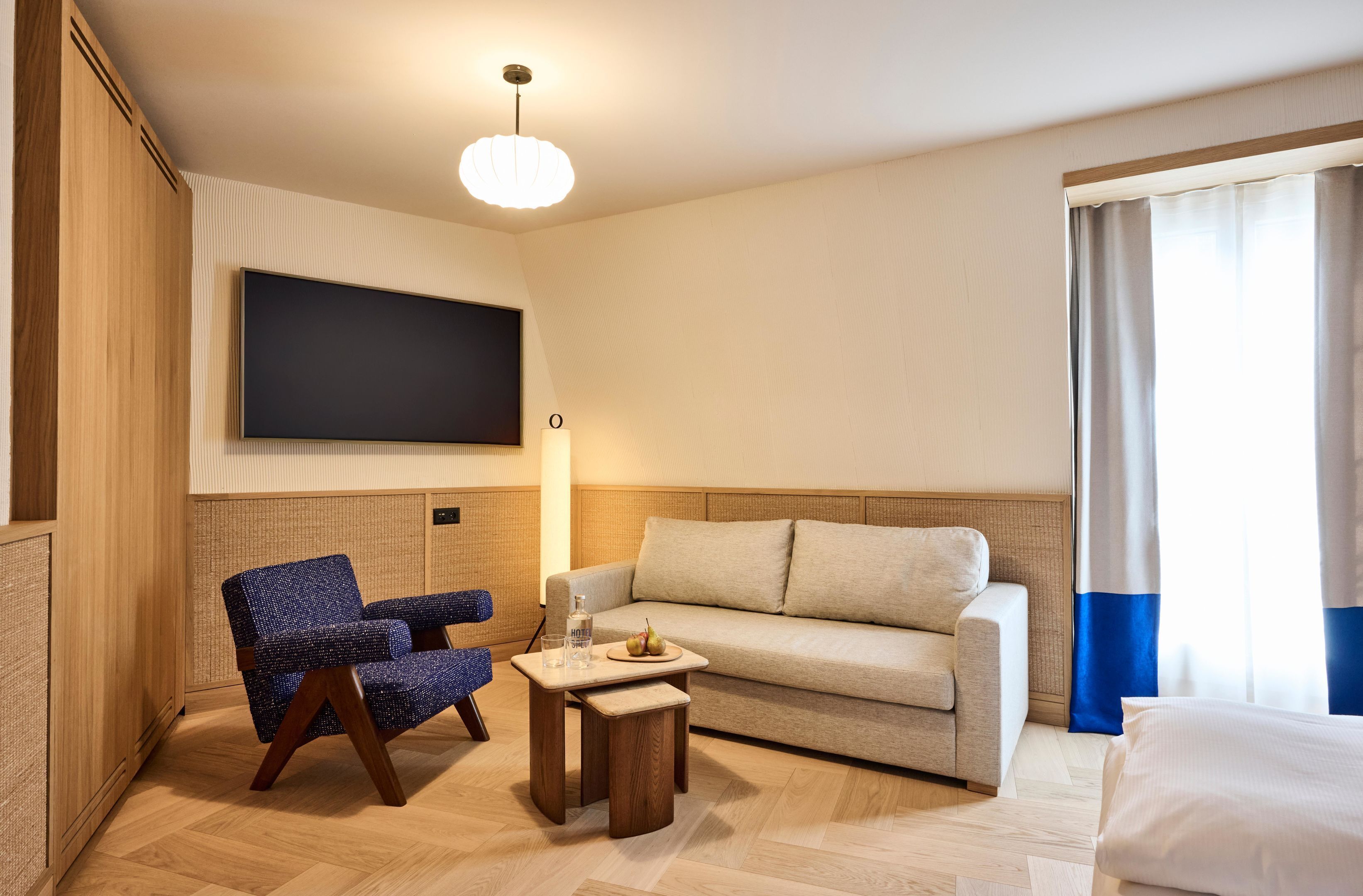 Une chambre d’hôtel équipée d’un téléviseur à écran plat, d’un canapé, d’un fauteuil, d’une petite table en bois et d’un lit.