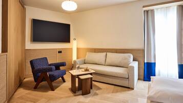 Une chambre d’hôtel équipée d’un téléviseur à écran plat, d’un canapé, d’un fauteuil, d’une petite table en bois et d’un lit.