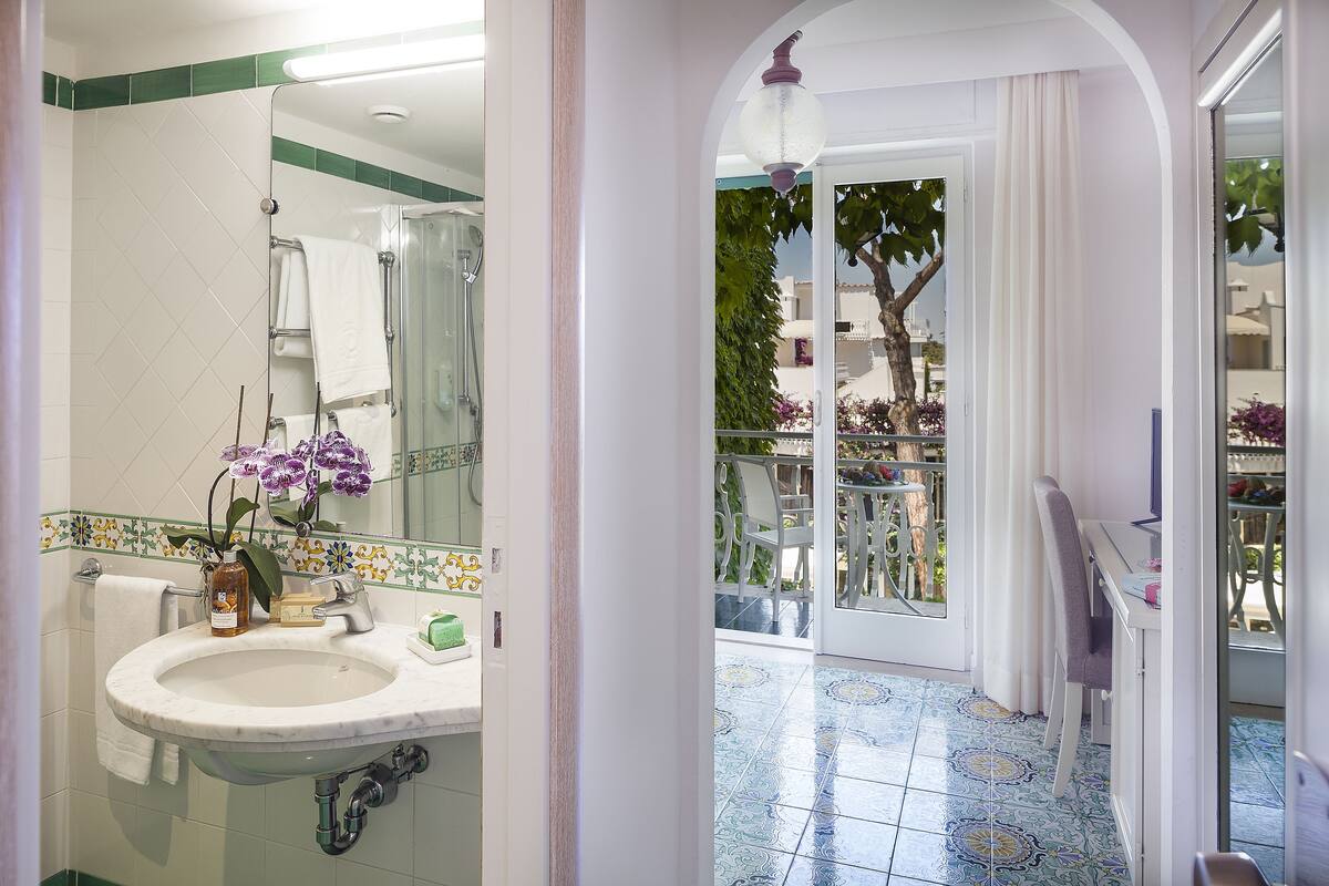 A bathroom with a sink, mirror, and a view of a balcony with outdoor furniture.