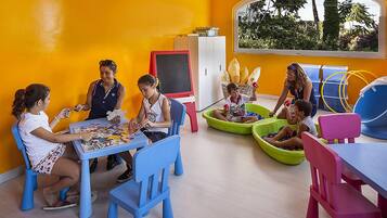 Una stanza dai colori vivaci con un'ampia finestra, una lavagna e bambini che svolgono diverse attività.