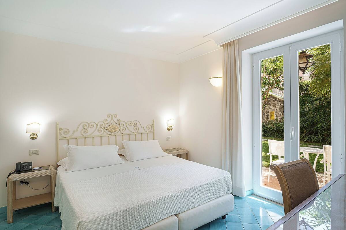 A hotel room with a bed, bedside tables, and a view of the outdoors through a sliding glass door.