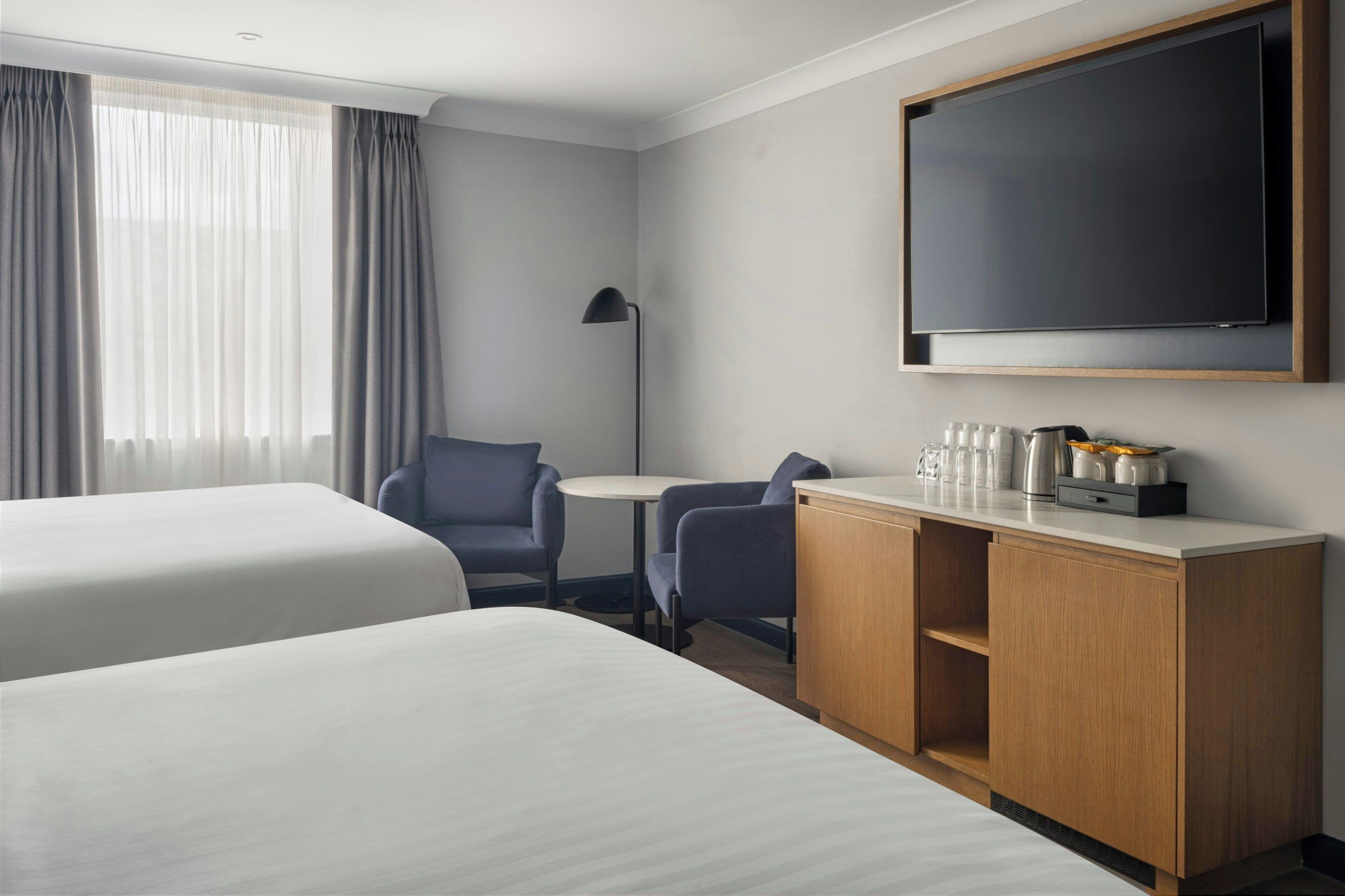 Ett hotellrum med två sängar, ett skrivbord, en stol, en TV och en minibar.