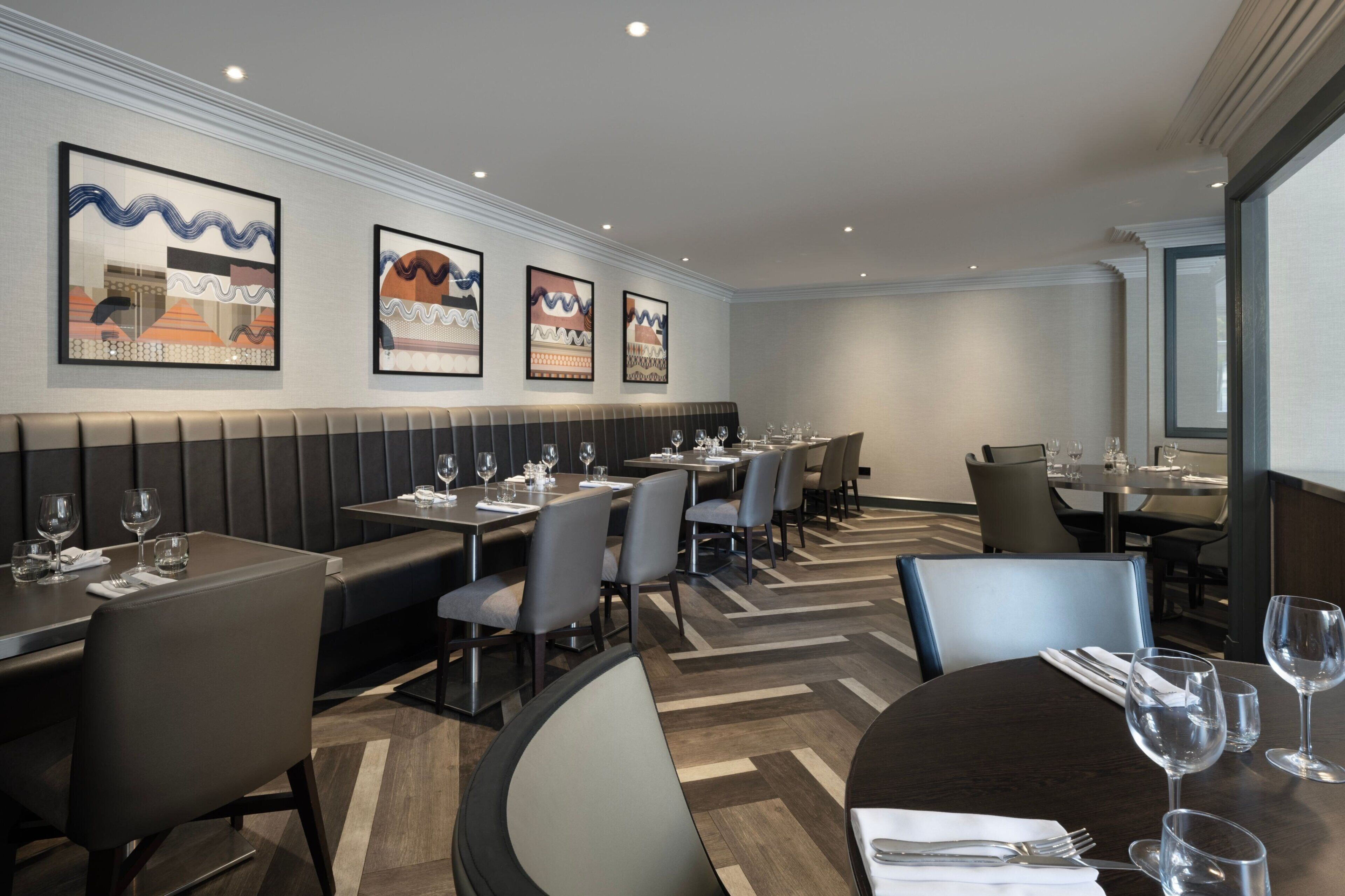 En moderne restaurant med både borde og siddepladser, billeder på væggene og et mønstret gulv.