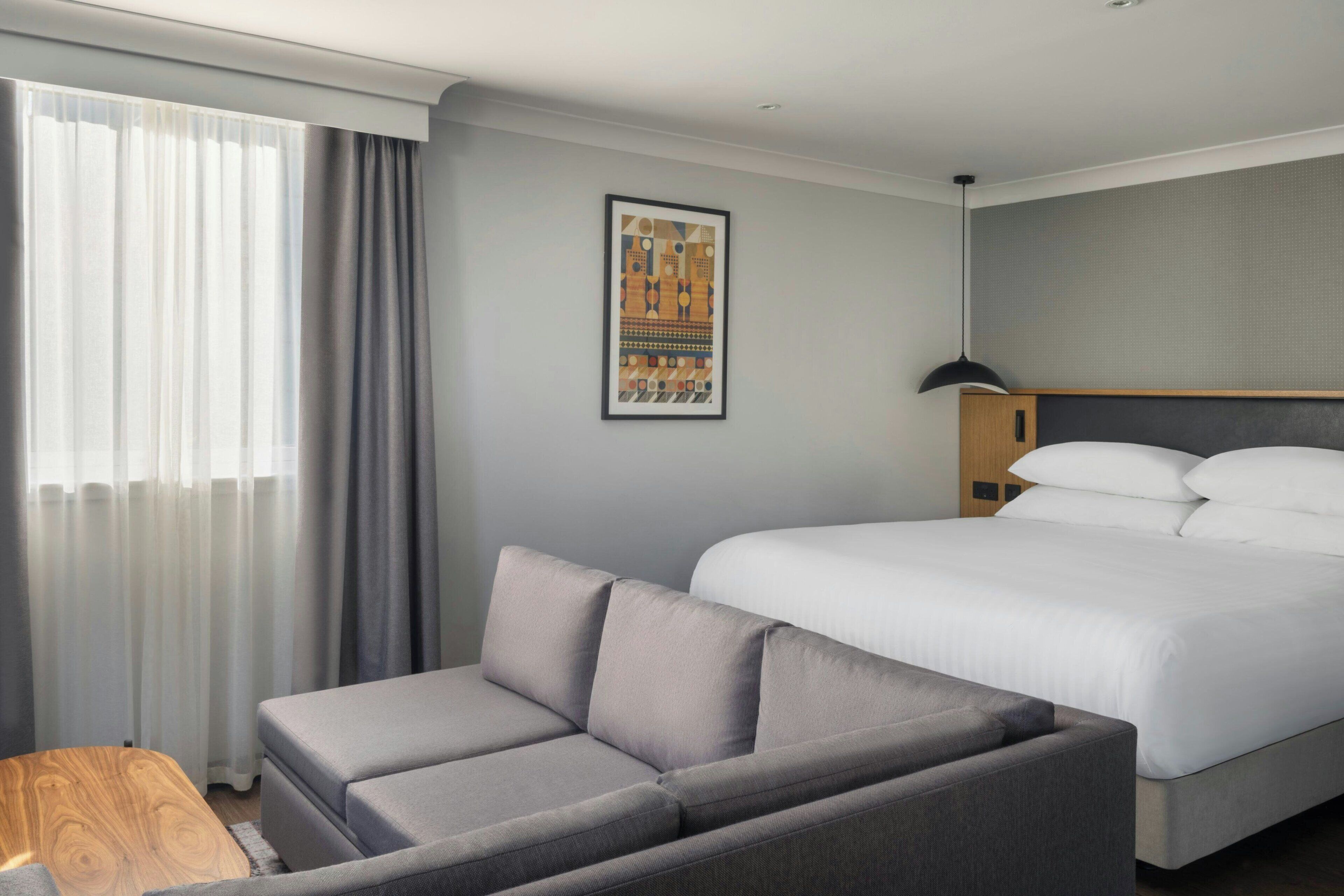 Ein Hotelzimmer mit einem Bett, einer Couch, einem Holztischchen und einem gerahmten Bild an der Wand.