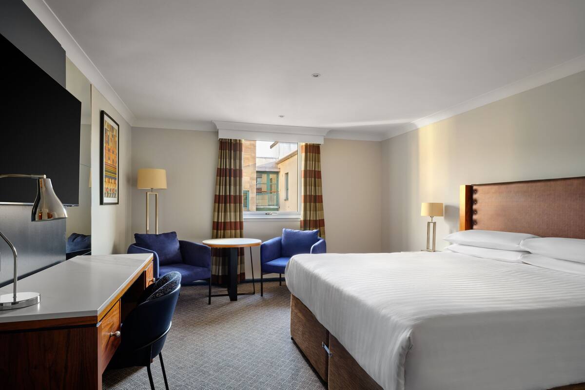 Una habitación de hotel con cama, escritorio, sillas y una mesita.