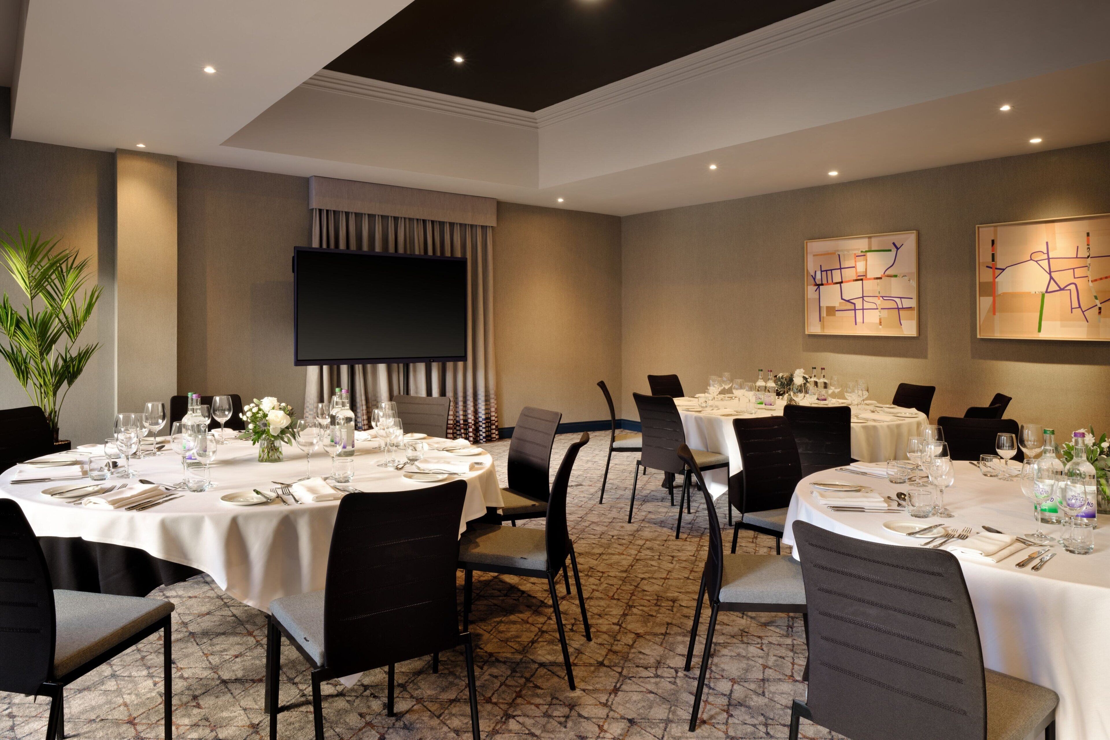A conference room with round tables, chairs, and a flat-screen TV.