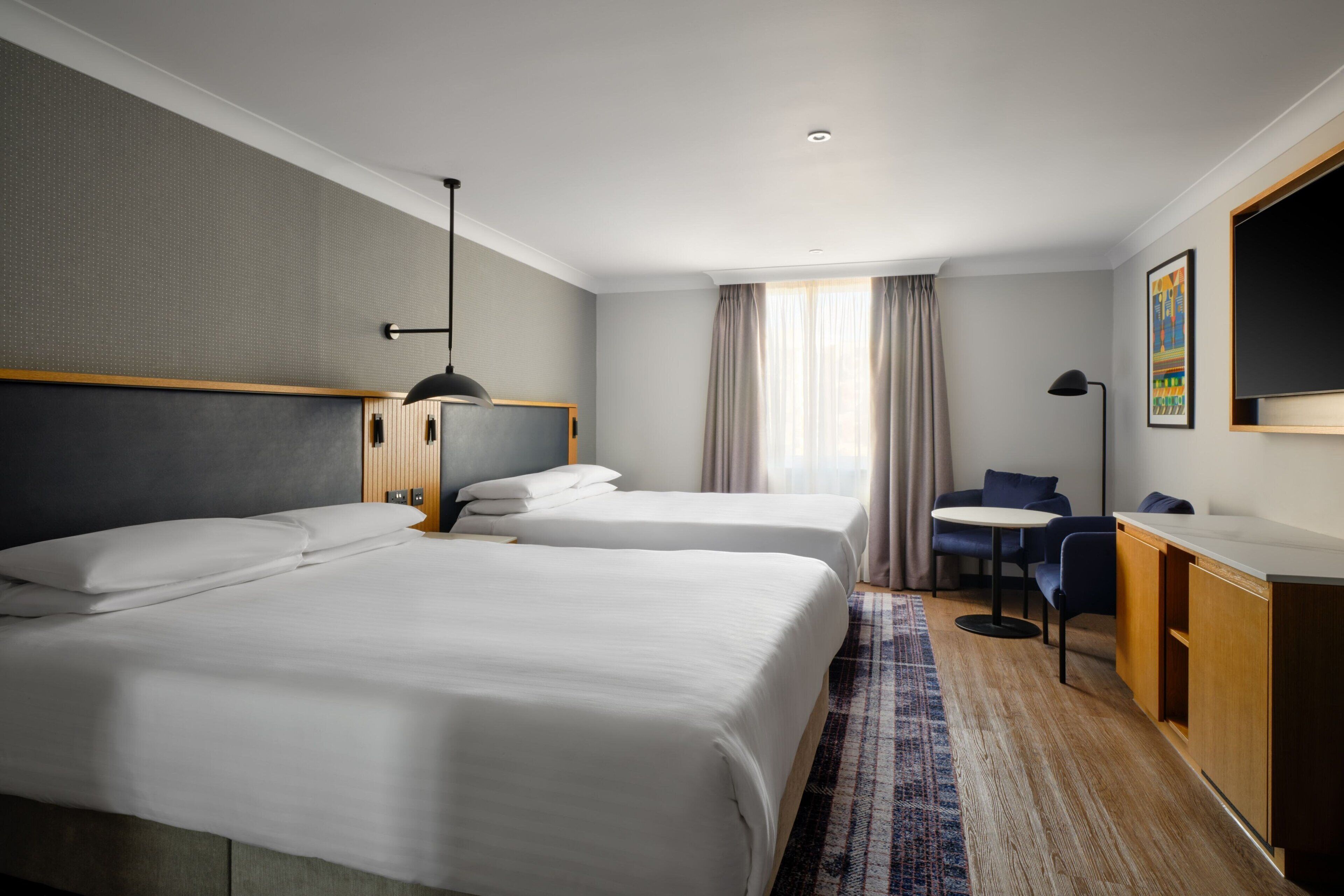 Une chambre d’hôtel avec deux lits, un bureau, une chaise et un téléviseur.